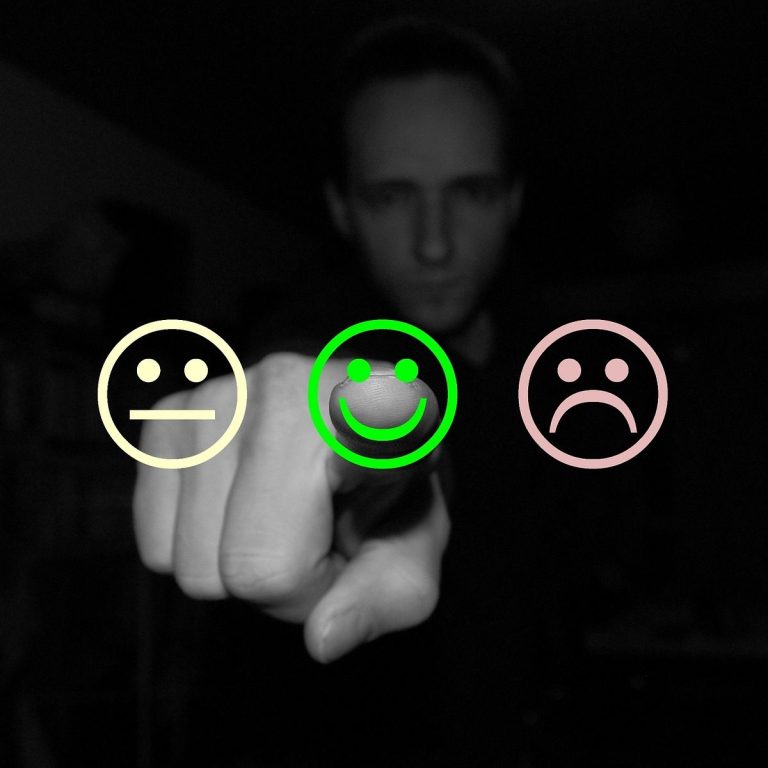 Picture of a man chosing between smiley, neutral and sad face. He points at the green smiley face.